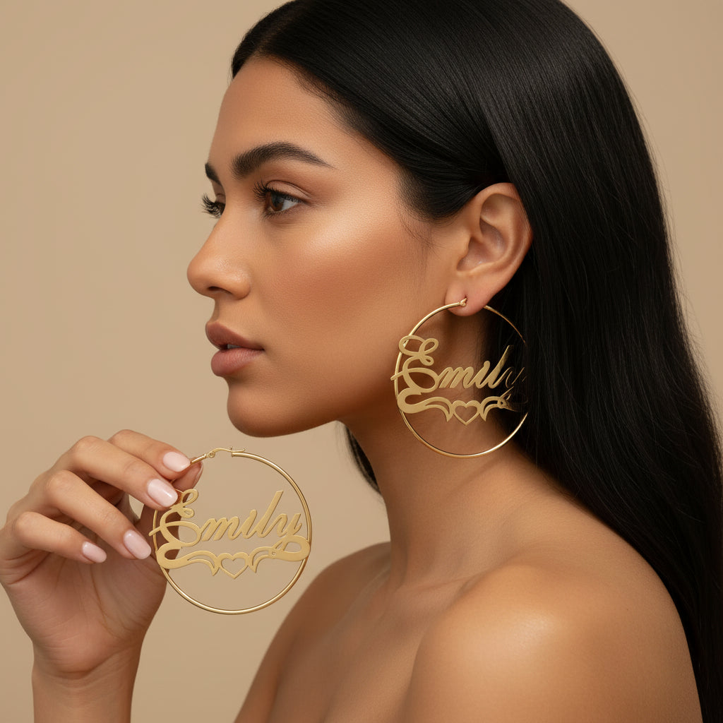 A close-up lifestyle shot of a blonde woman wearing large gold hoop earrings with the name 'Emily' and small hearts cut out, while holding one earring in front of her face against a neutral beige background.