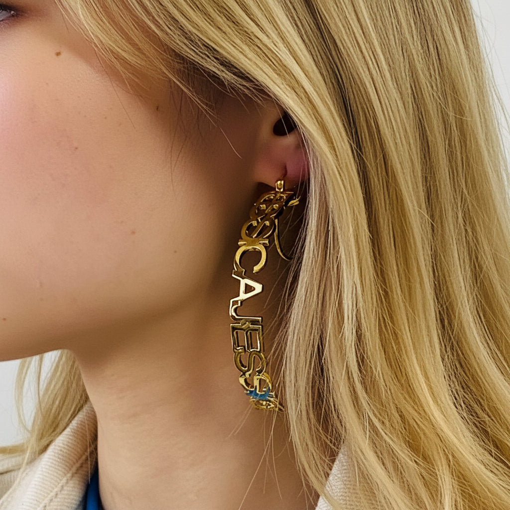 Close-up of a person wearing a gold Guess earring with a straw hat in the background